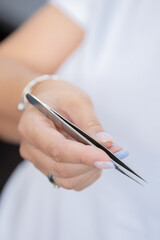 Closeup Eyelash extension master holds tweezers in hands