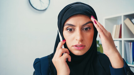 stunned muslim businesswoman in hijab talking on cellphone in office