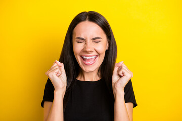 Photo of amazed funky lady raise fists close eyes open mouth wear black t-shirt isolated yellow color background