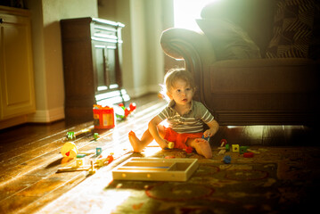 Little boy playing with toys on floor with autumn sunlight creating warm fall colors.