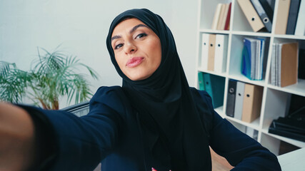 young muslim businesswoman pouting lips while taking selfie