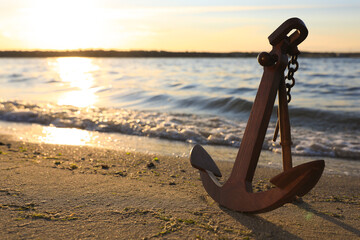 Wooden anchor on shore near river at sunset - obrazy, fototapety, plakaty