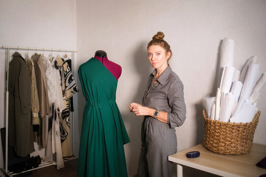 concept of small business. woman seamstress tailor designer pins fabric on mannequin against background of atelier.