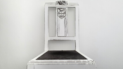 Rustic wooden chair painted by hand in white. Countryside decoration. Chair from the front in the picture with white wall in the background. Rustic and minimalist design.