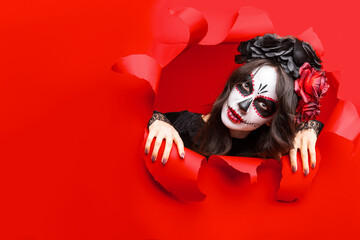 Girl with creative sugar skull makeup with wreath of flowers on head, wide isolated red paper hole...