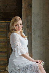 Fototapeta premium Boudoir photo of the bride in the morning. A beautiful portrait of a young blonde woman in a white coat sitting by the window.