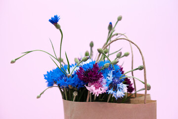 summer bouquet of colored cornflowers in disposable paper bag on pink background