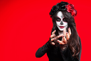 Girl with creative sugar skull makeup with a wreath of flowers on head, wide isolated on red background. Holiday concept Dia De Los Muertos  on poster for Halloween party or La Calavera Catrina.