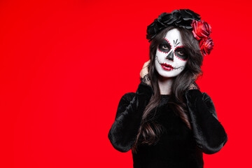 Girl with creative sugar skull makeup with a wreath of flowers on head, wide isolated on red background. Holiday concept Dia De Los Muertos  on poster for Halloween party or La Calavera Catrina.