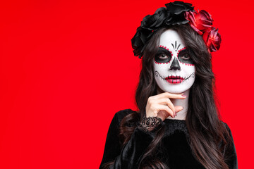 Girl with creative sugar skull makeup with a wreath of flowers on head, wide isolated on red background. Holiday concept Dia De Los Muertos  on poster for Halloween party or La Calavera Catrina.