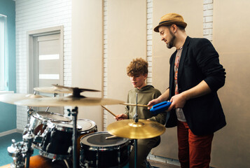 The teacher shows the boy how to play the drums. Lesson at the music school. - obrazy, fototapety, plakaty