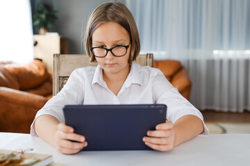 Focused gen Z schoolgirl engaged in homeschooling, watching online learning lecture on laptop at home. Kid attending remote virtual school class, listening to teacher.