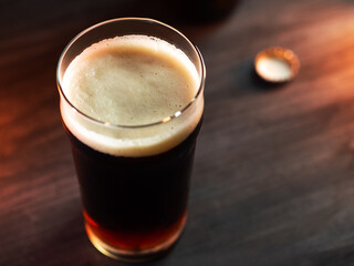 A glass of dark beer on a black wooden table, top view. Orange backlight