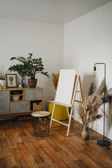 Home art studio interior. Easel with white canvas and brushes in the interior of the room. Concept of hobby drawing, canvas mockup.