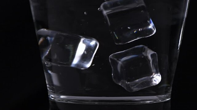 Slow motion of pouring ice cube into glass on black background, beverage concept