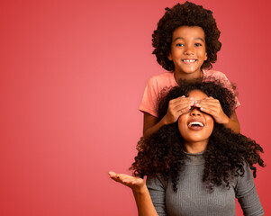 African American boy holding his mother closed eyes. Red background. Mothers Day. Brazilian family.