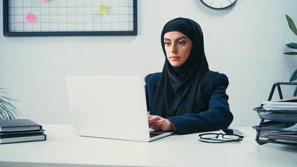 Young muslim woman in hijab using laptop in office