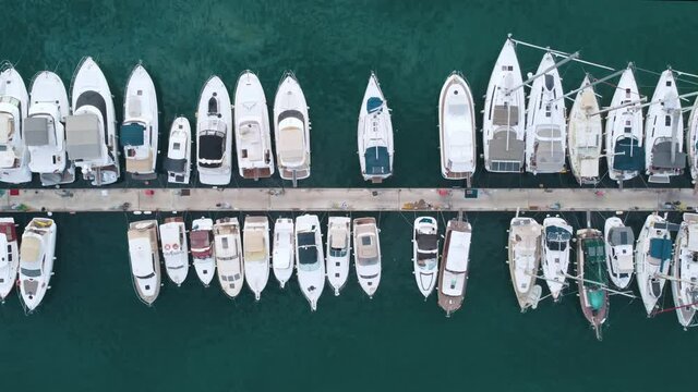 Flying over a marina with boats and yachts. Aerial top view of Luxurious boats are moored at the pier, slowly swaying on the waves.	