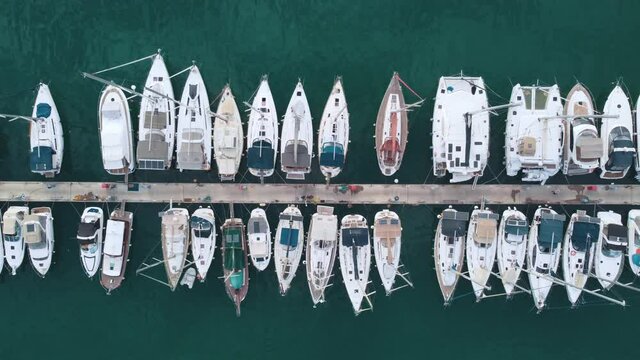 Flying over a marina with boats and yachts. Aerial top view of Luxurious boats are moored at the pier, slowly swaying on the waves.