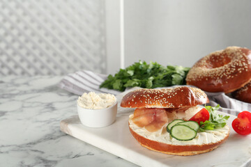 Delicious bagel with cream cheese, jamon, cucumber, tomato and parsley on white marble table. Space for text