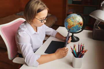 Fototapeta premium Schoolgirl engaged in homeschooling, watching online learning lecture on laptop at home. Kid attending remote virtual school class, listening to teacher. Remote learning at home with technology