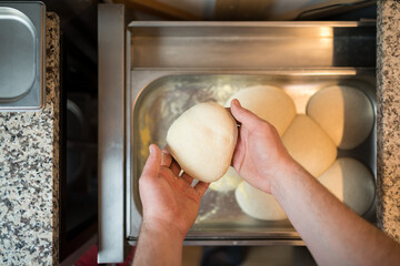 The chef takes a pizza blank from the baking sheet of the refrigerator drawer with his hands.