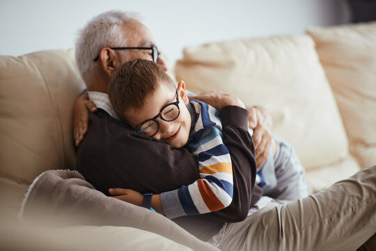 Happy little boy hugs his grandfather who is relaxing on the sofa at home.