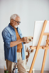 Fototapeta premium Senior artist enjoys while painting on canvas at his home studio.