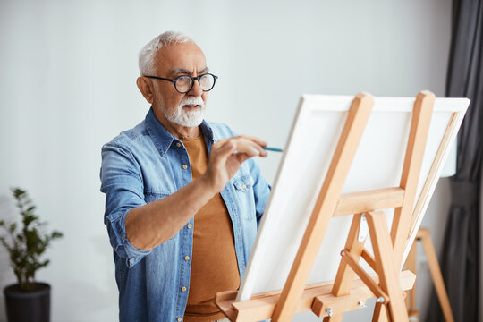 Senior artist paints on canvas at his home studio.