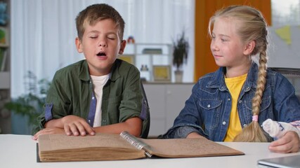 child reads book using his hands at home, blind boy learns while sitting with his sister with plaster cast on arm - Powered by Adobe