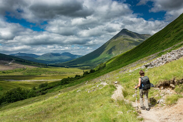 Along the West highland Way in Scotland. A hiker walks on the hiking trail in a hilly landscape dominated by the Beinn Dorain. - 458076306