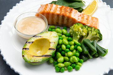 Salmon steak with beans, broccoli and fried avacodo on a plate. on a gray background.