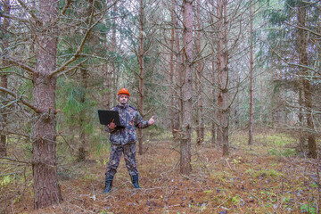 Forest engineer works in the forest with a computer. An ecologist in a young forest holds a...