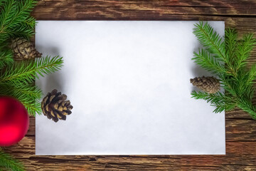 An empty space for the text. A blank white envelope, Christmas tree branches, cones, a Christmas ball on a woody background.