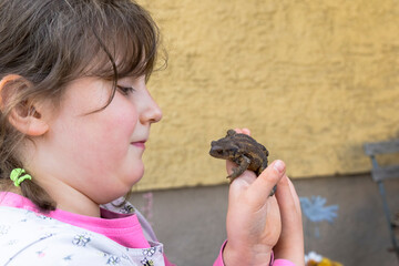 A little girl is happy about a toad in his hand