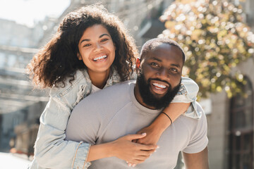 Happy african romantic couple friends piggyback walking outdoors spending time on romantic date....
