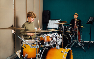 The boy plays the drum kit. Music lesson with teacher.