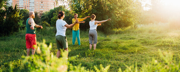 The coach conducts a warm-up. Group learning qigong in nature. - obrazy, fototapety, plakaty