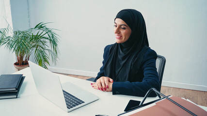 joyful muslim businesswoman looking at laptop in office