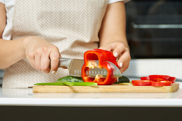 Woman in a modern kitchen cuts vegetables with a knife. Cooking something healthy and delicious