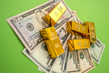 on a bright green background lie dollar bills with gold bars on top of them