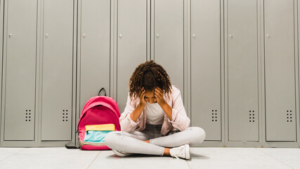 Troubles at school. Lonely sad african-american schoolgirl crying at school hall. Social exclusion...