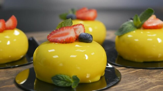 mousse round yellow cakes filled with mirror glaze with strawberries, blueberries and a mint leaf, close-up, rotate. Confectionery
