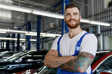 Strong happy young technician car mechanic man in denim blue overalls white t-shirt look aside hold...