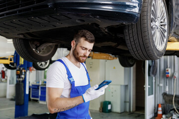 Young male professional technician mechanic man wears denim blue overalls t-shirt use hold mobile...