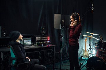 Recording songs in a music studio. Woman singer with headphones and sound producer.