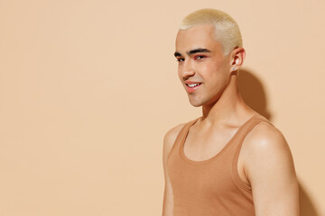 Side view young seductive fun blond latin hispanic gay man 20s with make up in beige tank shirt looking camera isolated on plain light ocher background studio portrait People lgbt lifestyle concept.