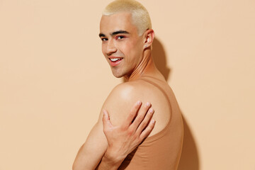 Side view young smiling trendy blond latin gay man 20s with make up in beige tank shirt hug himself...