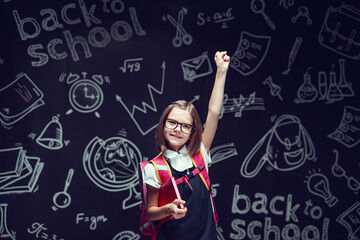 Happy schoolgirl in glasses preparing to go to school holding book raising hand up. Back to school 