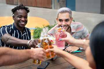 Two cool casual happy friends having a drinks in a terrace. Black male and gender fluid friend. Celebrating with a toast outdoors. . High quality photo